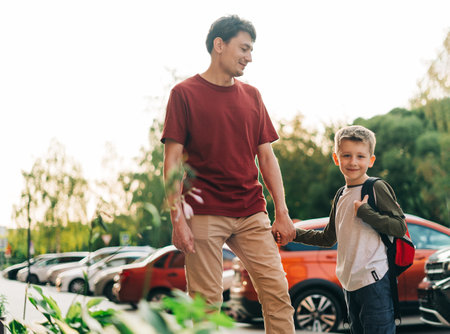 Happy father and kid son going to classes. Parent take child boy to school in first grade. Pupil of primary school go study with backpack outdoors in city street. Beginning of lessons. Back to school.の写真素材