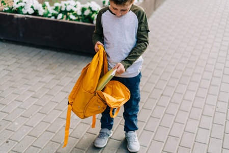 Back to school. Cute child packing backpack, holding notepad and training books going to school. Boy pupil with bag. Elementary school student going to classes. Kid walking outdoor on the city street.の写真素材