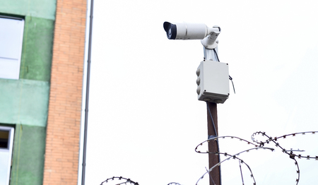 Camera video surveillance on the building background mounted on a brick wall, fenced with barbed wire.の写真素材