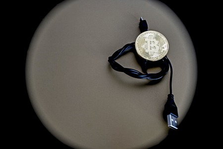 Digital kriptonite bitcoin with a USB cable on a bronze background.