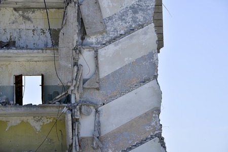 The remains of the destroyed concrete wall of a large building with open doors on a high floor against the sky. Background.の写真素材