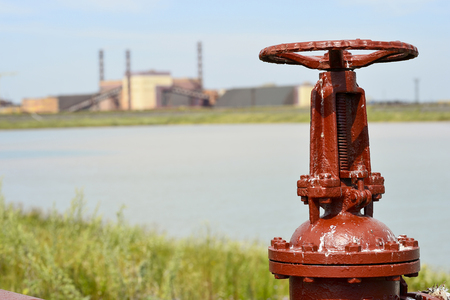 The valve from the pipeline against the background of the factory and an artificial lake.の写真素材