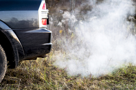 The back of the black car with the emission of smoke from the exhaust pipe on the background of nature. The concept of environmental pollution by vehicles.の写真素材