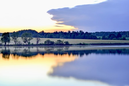 Twilight with reflection of the evening sky in water of the lake tightened by a big cloud. Background.の写真素材