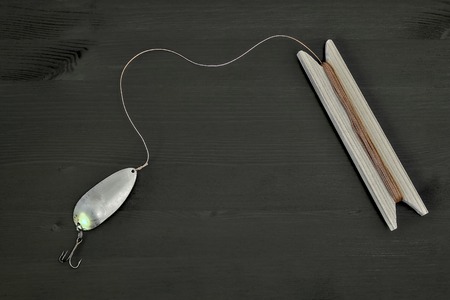 Homemade spoon spinner with a cord tied to it and wound on a wooden reel. Ancient concept of...