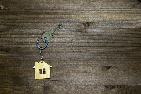 Symbol of a bamboo house with a metal key on a brown vintage wooden background. Lighting gradient. The concept of selling real estate with the transfer of ownership.の写真素材