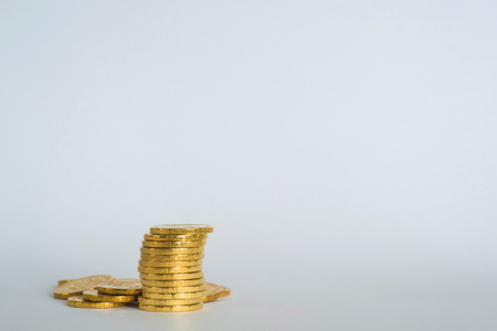Yellow shiny coins are stacked on a light gray blue background