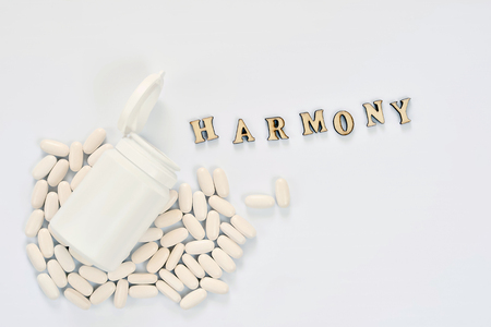 A white bottle with an open lid and the inscription harmony lies on oval tablets on a pale blue background.の写真素材