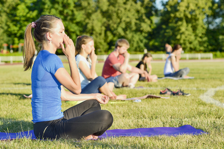 Young woman in a blue shirt doing yoga in a group at the city stadium, Russia, Kursk region, Zheleznogorsk, June 2018. The concept of a healthy lifestyle.のeditorial素材