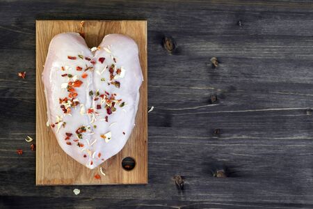 Chicken breast sprinkled with dried vegetables lies on a bamboo cutting Board on a wooden rustic dark background. Copy space, top view, space for text.の写真素材