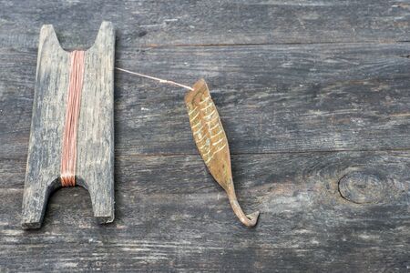 Ancient tackle for vertical flashing predatory fish. Copper forged spinner and reel with rope on wooden rustic background. Text space.の写真素材