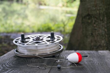 Fishing reel with fishing line, red and white float, hook and sinker on wooden table on natural background. The concept of classic fishing tackle. Text space.の写真素材