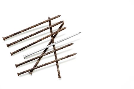 Metal shiny sharp nail in the center of a pile of old rusty nails isolated on white background.の写真素材