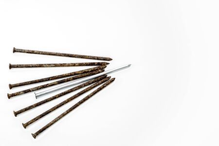 Metal shiny sharp nail in the center of a pile of old rusty nails on a white background.の写真素材