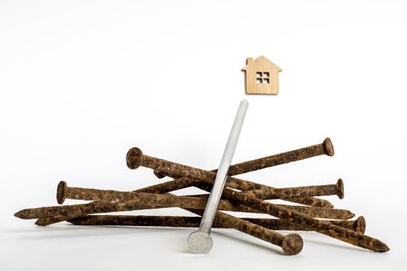 A shiny metal nail close-up lies on a pile of old rusty nails and is aimed at the house symbol on a white background.の写真素材