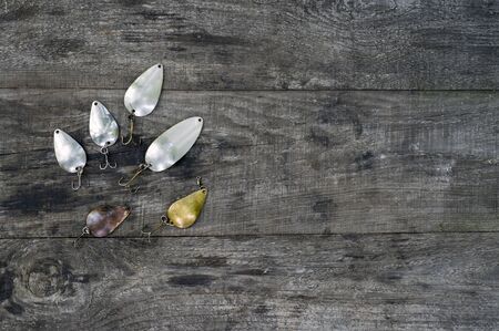 Metal spinners in the shape of a spoon of different colors for catching a predator on a vintage wooden background. The concept of choosing bait for different fishing conditions. Copy space. Flat lay.の写真素材