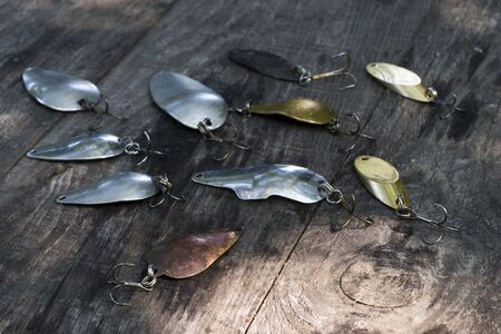 Metal spinners in the shape of a spoon of different colors for catching a predator on a vintage wooden background. The concept of choosing bait for different fishing conditions. Copy space.の写真素材
