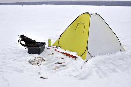 Winter yellow fishing tent fixed on the ice with all the necessary attributes for fishing. Catch roach lying in the snow in front of the tent.の写真素材