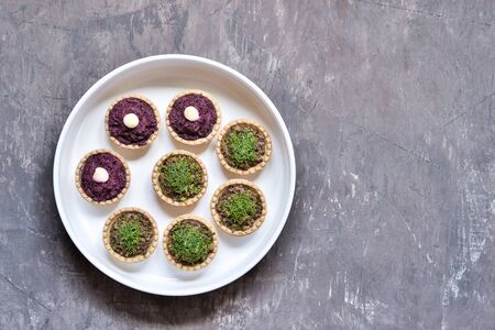 Tartlets stuffed with beetroot and mushroom mince sprinkled with dill in a white plate on a worn...