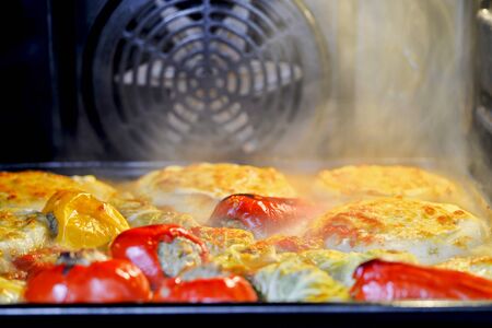 Assorted stuffed peppers, stuffed cabbage and zucchini on a baking sheet in the oven.の写真素材