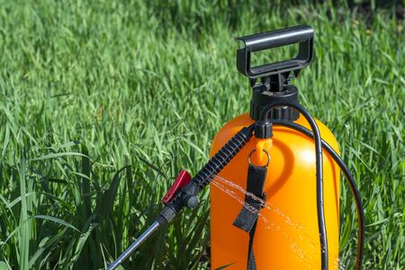 Jets of aqueous chemical solution gush from the black plastic handle of the orange sprayer. Background.の写真素材
