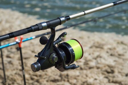 Fishing carp reel close-up on the background of water and fishing rods on stands in a bright Sunny...