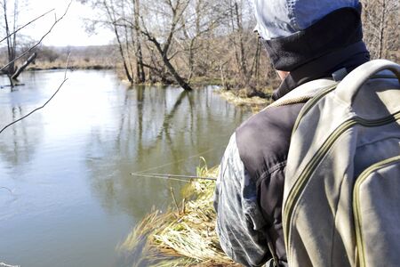 A male angler catches a predator spinning in a cold river. Rear view.