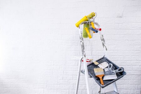 Painted stepladder with black tray, paint bucket, set of brushes and multi-colored spatulas for repair in the form of an abstract art easel shape. The concept of creative approach to interior design.の写真素材