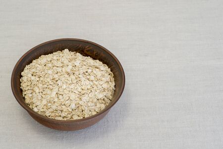 Oatmeal in a brown ceramic bowl on a linen tablecloth. The concept of cooking natural healthy food