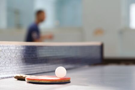 A racket with a white ball lies on a tennis table on the background of a tennis net and an athlete...