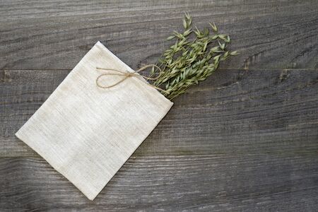 Small linen bag knotted with jute twine with green ears of oats on a wooden volumetric background....