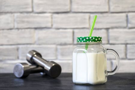 White protein cocktail in a mug on the background of dumbbells and a white wall decorated with bricks. Background. Concept of sports nutrition and protein diet.の写真素材
