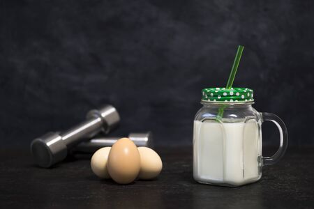 Protein white cocktail in a mug and chicken eggs on a dark background with dumbbells. Background. Concept of sports nutrition and protein diet.の写真素材