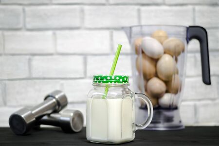 White protein cocktail in a mug on the background of a blender bowl with chicken eggs and dumbbells on a building brick wall background. Background. Concept of sports nutrition and protein diet.の写真素材