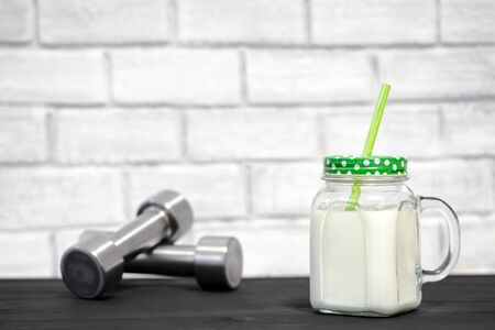 White protein cocktail in a mug on the background of dumbbells and a white wall decorated with bricks. Background. Concept of sports nutrition and protein diet.の写真素材