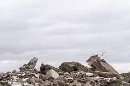A pile of large gray concrete fragments with protruding fittings against a cloudy sky.