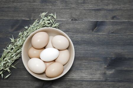 Chicken eggs in a light wooden bowl with oats on a dark wooden table. Background. The concept of...