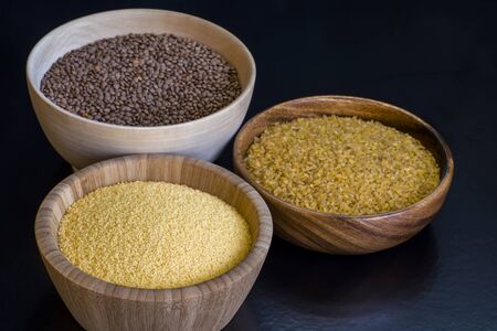 Cereals couscous, bulgur, red lentils in wooden bowls on a black background. Concept of Eastern cuisine dishes.の写真素材