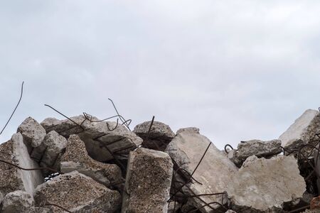 A pile of large gray concrete fragments with protruding fittings against a cloudy sky. Remnants of the destruction of a large concrete building. Building background.の写真素材