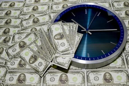 The concept of time is money, a wall clock against a pile of thousand-dollar bills.の写真素材