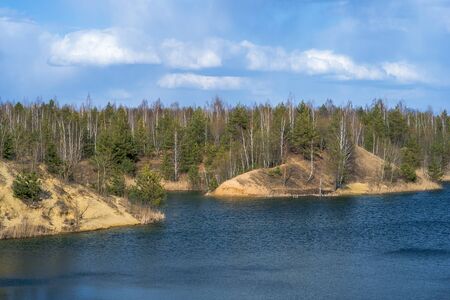 Forest lake with dry yellow coastal vegetation in early spring, blue water and cloudy picturesque sky. Background.の写真素材
