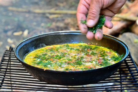 A man's hand in a blurry motion sprinkles dill greens on an open-air fried egg in a frying pan.の写真素材