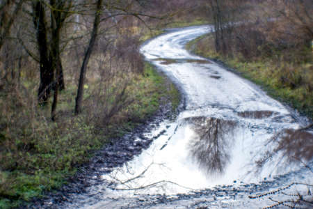 Blurred soft background. A winding village road with a large puddle in the foreground stretches away into.の写真素材