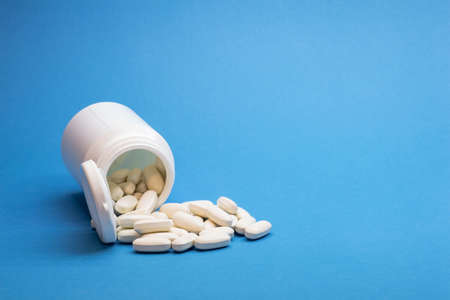 White bottle with a pile of oval tablets on a blue background. background.の写真素材