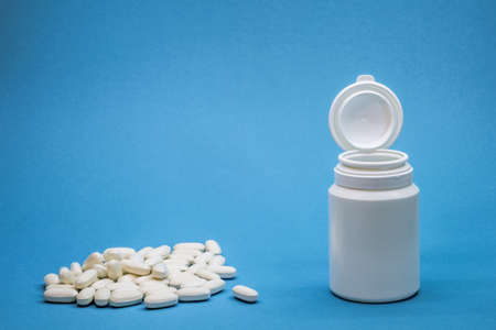 White bottle with a pile of oval tablets on a blue background. Backgroundの写真素材