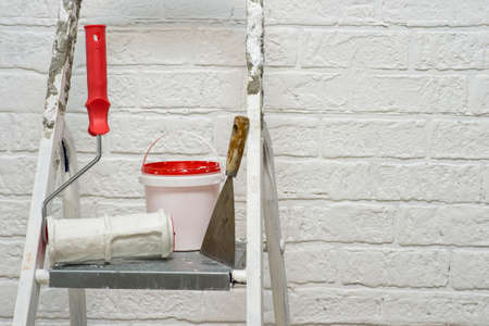 A spatula, bucket and textured roller under the brick stand on a metal stepladder on the background...