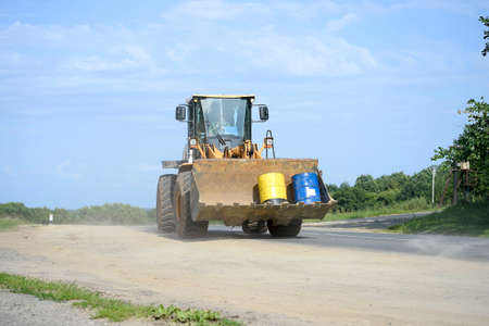 A large yellow wheeled tractor with a bucket carries two tanks on the highway. Transportation of cargo, constructionの写真素材