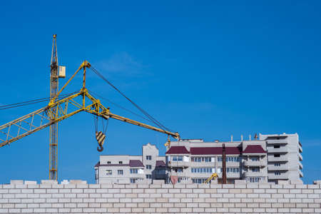 Cranes on the background of a brick house under construction with a blue sky and a brick wall in the foreground. background.の写真素材