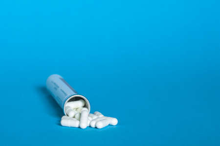A bottle with a bunch of white capsules of tablets on a blue background.の写真素材