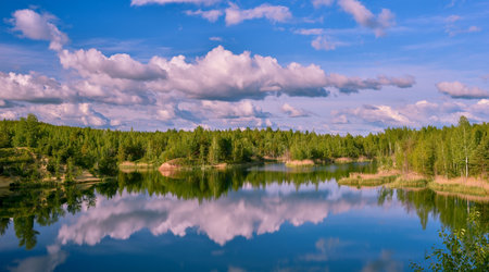 Lake with banks in the bright spring green of the forest with a reflection of the blue sky with...